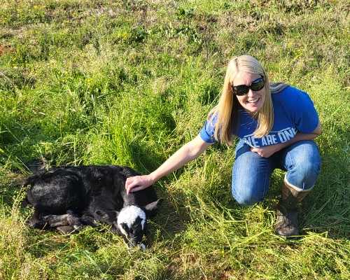 Anna kneeling in the pasture beside a black calf
