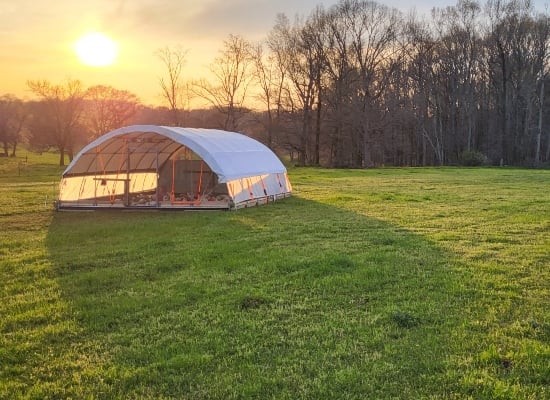 A white chicken-run shelter on green pasture at sunset